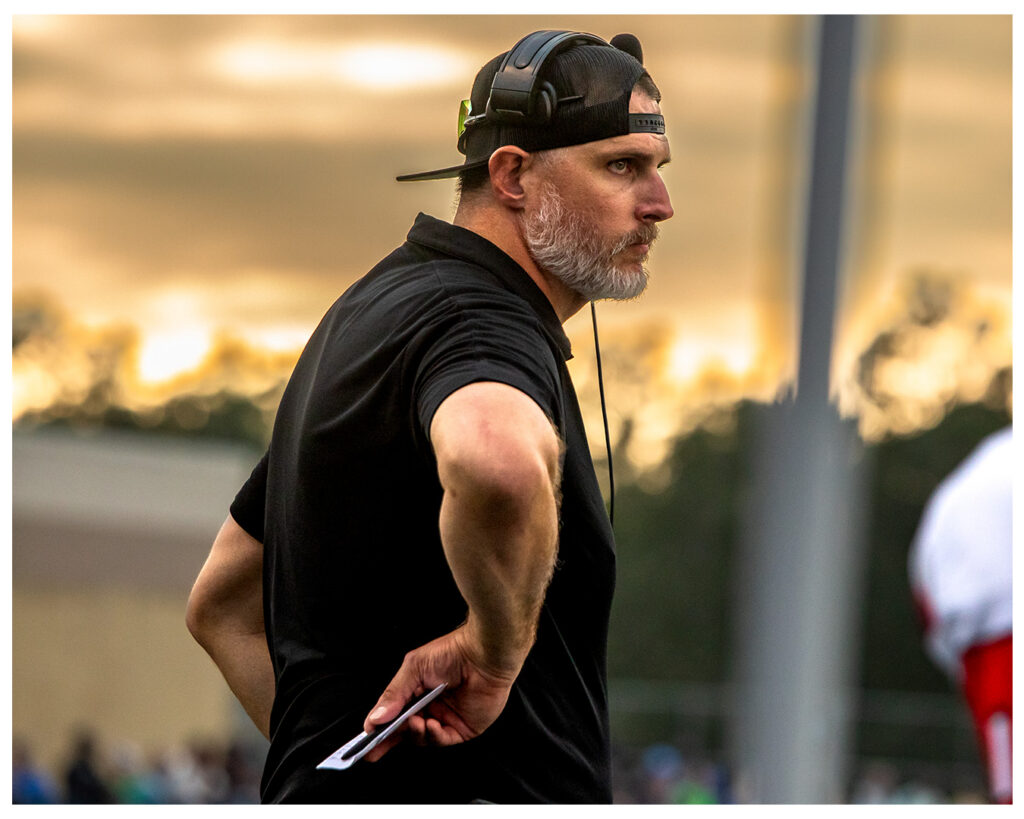 Coach Nate Garner on the sideline with headset at golden sunset