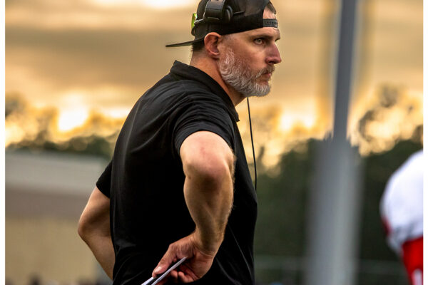 Coach Nate Garner on the sideline with headset at golden sunset